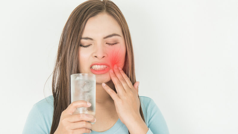 young woman suffers from her tooth sensitive to cold water