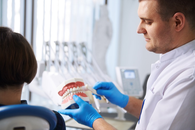 Oral hygiene and teeth protection. Male dentist with jaw model and toothbrush showing how to clean teeth to female patient.