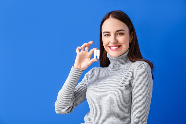 Beautiful smiling young woman with plastic tooth on color background