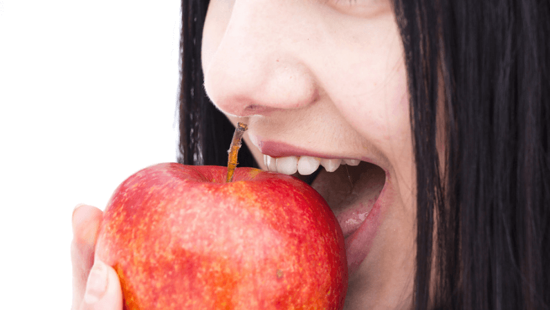 Happy and Healthy, natural organic portrait of attractive smiling girl holding green apple in her hand over blue background.
