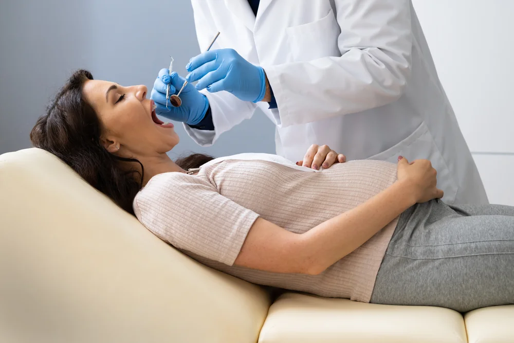 Dentist Treating Teeth Of Young Pregnant Woman Patient Lying In Clinic