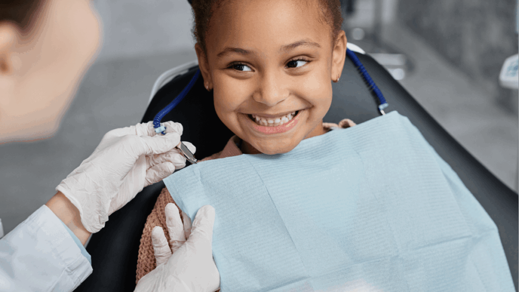 Portrait of smiling little girl in dental chair with nurse preparing her for teeth check up