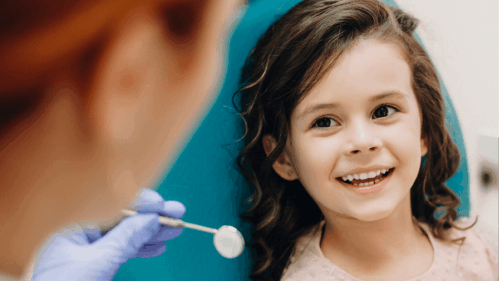 Lovely little kid smiling while talking with the pediatric dentist after doing a tenth examination
