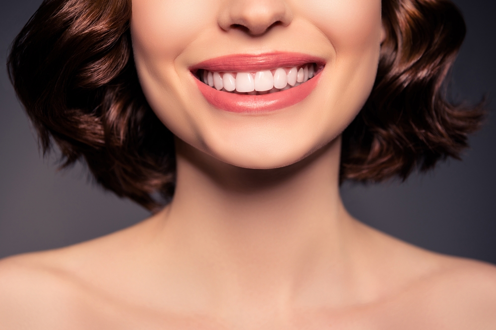 Cropped photo of smiling female naked shoulders showing perfect teeth