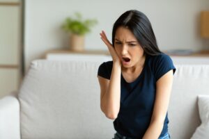 Woman holding her cheek in pain from a dental emergency at home.