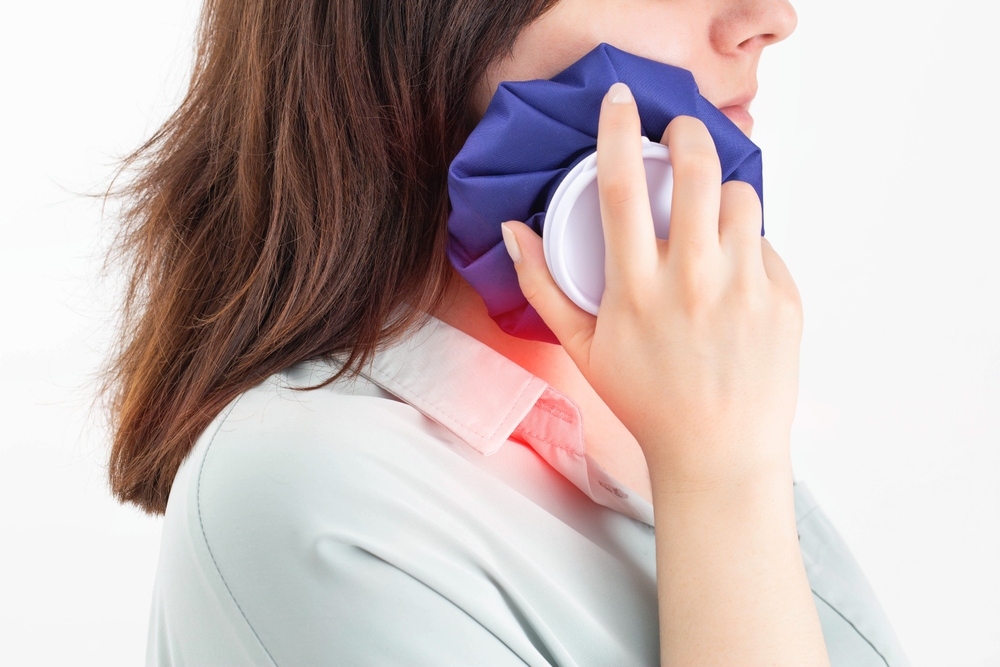 A girl attaches a medical bag with cold to the swelling on her cheek after removing a wisdom tooth.